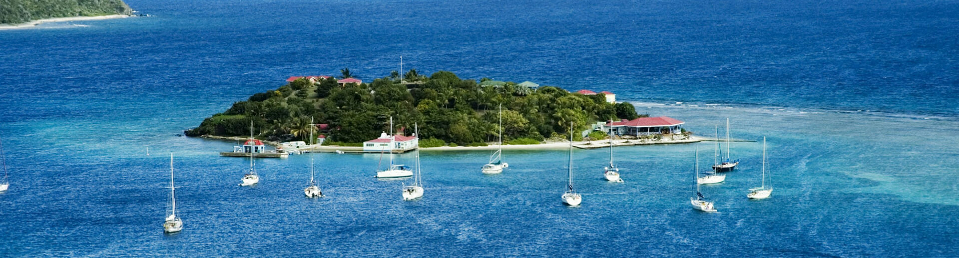 Charming view of Marina Cay in the British Virgin Islands – A yacht anchored in the tranquil waters, surrounded by lush tropical scenery and vibrant blue skies, showcasing the beauty of this popular sailing holiday destination.
