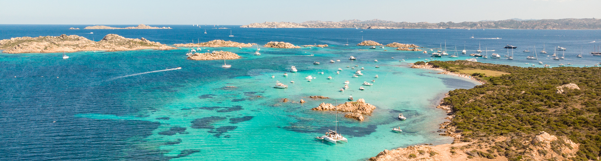 Stunning aerial view of the Sardinia sailing itinerary near the Maddalena Archipelago – A yacht navigating the crystal-clear waters, surrounded by pristine beaches and lush islands, showcasing the natural beauty of this idyllic sailing destination.